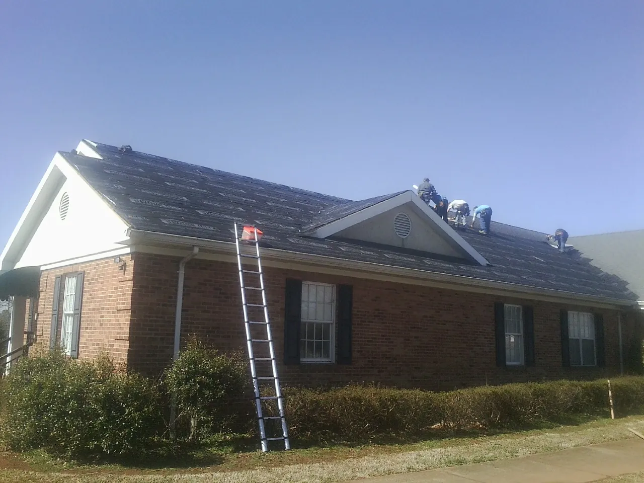 Crew tearing shingles off a brick ranch roof with a ladder set — Metal Roof Repair work by our crew in Reeseville