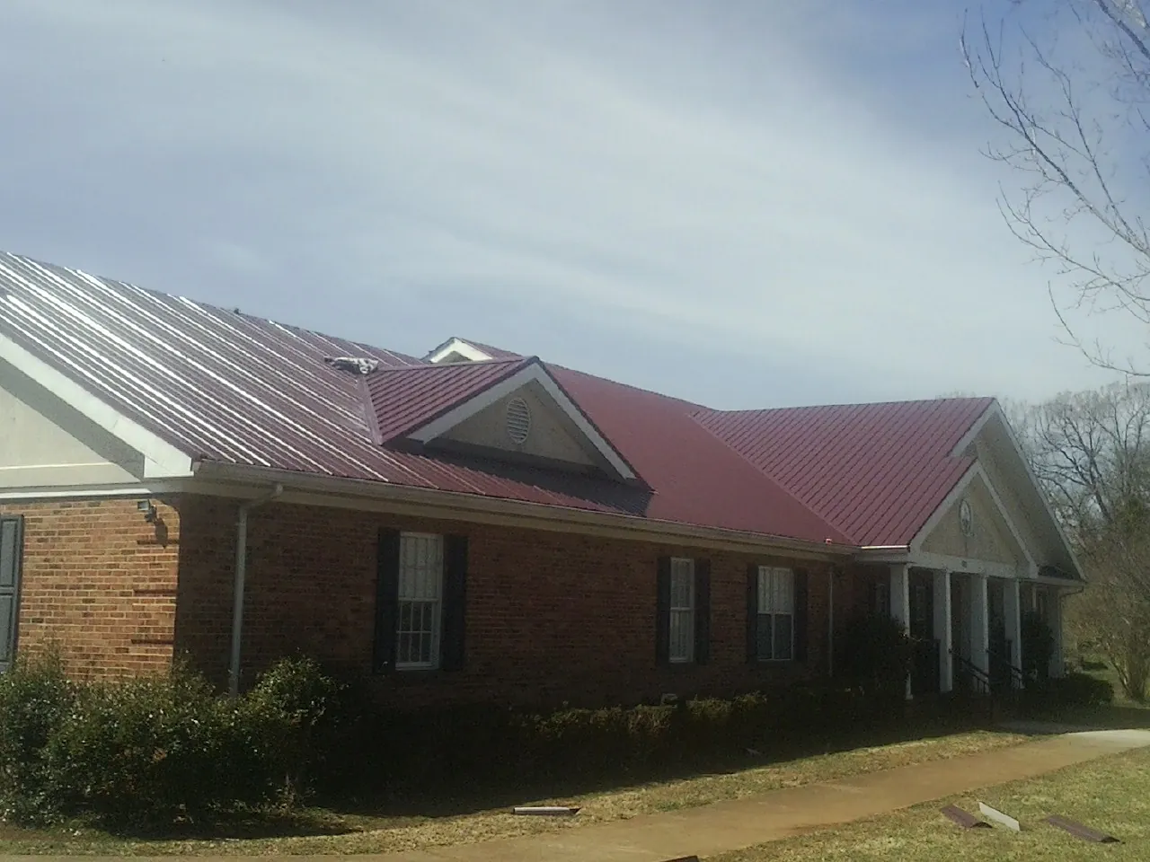 Red metal roof with gabled entries on a long brick building, from a Hail Damage Roof Repair job in Reeseville