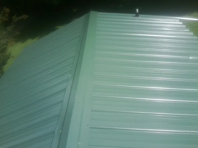 New green metal panels meeting at the ridge of a roof — Flat Roof Repair work by our crew in Reeseville